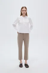 Blusa blanca de viscosa con cuello a la base, mangas largas abullonadas con puños ajustados, detalles de volados, encaje y botones frontales.