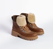 Borcegos de cuero vacuno en tonos marrón, con diseño de caña media y cuello con forro de piel sintética negra. Presentan cordones marrones, ganchos metálicos para ajuste y suela de goma tipo track con plataforma.