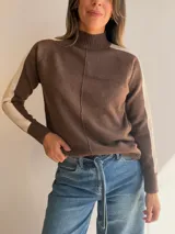 Sweater de tejido de punto en color beige con cuello alto y costura central vertical. Presenta mangas ranglan con una franja lateral en color marrón oscuro que genera contraste, y terminaciones en tejido acanalado en puños y ruedo.