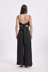 Pantalón negro de tiro alto, corte ancho y fluido, con detalle de cruce o fajín envolvente en la cintura.