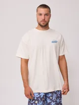 Remera de algodón color crema, corte oversize, con estampado frontal pequeño de la marca Rusty en azul.