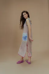 Vestido largo de tejido calado color beige, con estampado de flores en tonos rosados, celestes y verdes. Presenta escote cuadrado con ribete azul y terminaciones con crochet fucsia.