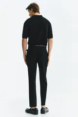 Pantalón sastrero de corte ajustado, color negro, con pliegues frontales, cierre de botón, bolsillos laterales y bolsillos traseros ribeteados.