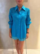 Camisa turquesa con diseño calado, cuello camisero, manga larga con puños anchos y cierre frontal oculto.