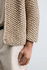 Cardigan de punto grueso color beige, con cuello pico, manga larga y cierre frontal de botonadura.