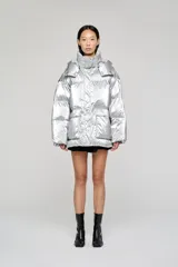 Campera puffer de corte holgado y acabado metalizado, con cuello alto envolvente, capucha desmontable y cierre frontal con botones. Presenta mangas amplias y bolsillos frontales con solapa.