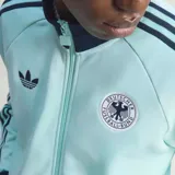 Campera deportiva adidas de la selección de Alemania, color verde agua con detalles en azul marino en cuello, puños y las icónicas tres tiras en las mangas. Presenta cierre frontal, logo del trébol de adidas en el pecho derecho y escudo de la federación alemana en el pecho izquierdo.