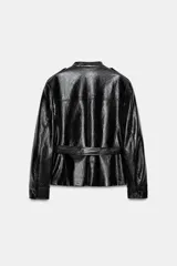 Cazadora efecto piel de Zara Woman Collection, en color negro. Cuenta con cuello redondo, manga larga, bolsillos de parche con solapa en el delantero y cierre frontal con botones forrados. Incluye un cinturón del mismo tejido para ajustar en la cintura.