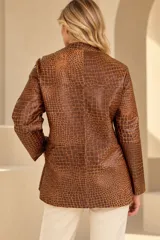 Camisa de cuero color marrón, de corte recto y largo medio, con cuello redondo a la base, cierre frontal con broches metálicos y bolsillos aplicados en los laterales.