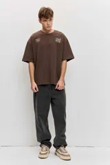 Remera marrón oversize de manga corta, con cuello redondo y pequeños estampados blancos en el pecho.