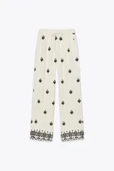Pantalón color crema de tiro medio con cintura elástica ajustable y bolsillos delanteros. Presenta bordados florales en negro y corte ancho.