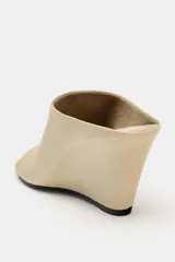 Sandalia tipo mule con tacón cuña, confeccionada en piel color beige. Presenta diseño destalonado, apertura frontal y punta cuadrada asimétrica.