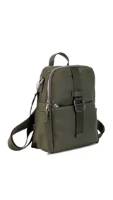 Mochila de tamaño mediano, color beige claro, con cuerpo principal de tela impermeable y detalles en simil cuero liso en la parte inferior y correas. Presenta un asa superior corta y correas ajustables para llevar al hombro o cruzada. Cuenta con un bolsillo frontal con cierre y un detalle decorativo de correa con hebilla metálica rectangular.