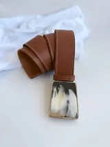 Cinto de cuero color tostado con hebilla rectangular de guampa con marco metálico. El broche suizo permite intercambiar la hebilla.