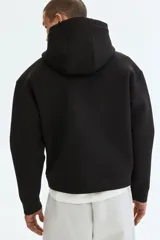 Canguro negro con capucha de doble capa, efecto neopreno, hombros caídos, bolsillo canguro frontal y puños y bajo anchos acanalados. Corte holgado.