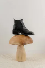 Botas tipo chelsea de cuero color marrón oscuro con acabado brillante. Presentan punta cuadrada con detalle de puntera metálica, elásticos laterales y taco cuadrado bajo.
