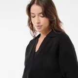 Sweater de punto en color negro, con cuello en pico y mangas cortas. Presenta un diseño de tejido acanalado y corte recto.