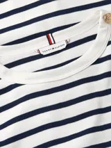Remera de manga larga Tommy Hilfiger con diseño de rayas horizontales en azul marino y blanco. Presenta cuello redondo y detalle de botones decorativos en tono dorado sobre los hombros. Incluye el logo de la marca bordado en el pecho.