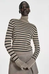 Jersey de punto liso en color beige, con cuello alto y manga larga con detalle de botones metálicos en los puños.