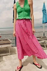 Falda midi con silueta evasé y estampado de cuadros en tonos fucsia y blanco. Presenta cintura elástica con lazo ajustable y detalle de borlas colgantes.