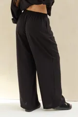 Pantalón largo negro de corte holgado, con cintura elástica fruncida y cordón ajustable delantero.