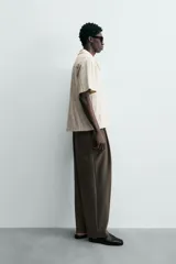 Polo de hombre color crema, de tejido texturado con rayas verticales en relieve, corte relajado, cuello bowling y cierre frontal parcial con botones.