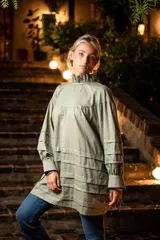 Camisa verde militar de algodón con cuello alto con volado, mangas largas con aberturas y tiras para atar, tablas en la parte inferior y cierre con tres ataduras.