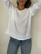 Remera blanca de manga larga con cuello redondo y detalle de tejido crochet en el dobladillo. Incluye un collar fino dorado como accesorio.