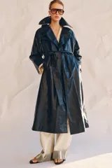 Trench oversize de efecto piel color azul marino, con cuello solapa, manga larga, bolsillos delanteros y cinturón ajustable del mismo tejido. Cierre frontal cruzado con botones y forro interior.
