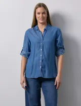 Camisa gris de tencel con cuello con solapa, escote en V y abertura central con botones. Largo de manga regulable con presilla y botón. Ruedo en espalda con tajo.