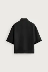 Camisa marrón de corte boxy fit, con tejido estructurado, cuello bowling, manga corta y un bolsillo aplicado en el pecho. Cuenta con cierre frontal de botones.
