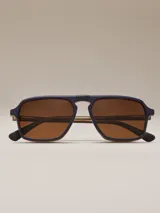 Lentes de sol con montura azul y lentes marrones. Diseño cuadrado con doble puente y patillas marrones con detalles a rayas.