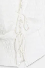 Top de manga larga con textura nido de abeja, escote en pico con detalle de volantes y cierre frontal mediante lazos ajustables.