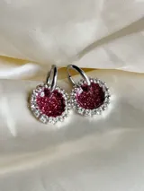 Aros colgantes con forma circular, hechos de resina color lila y borde de strass plateado. El aro es de acero quirúrgico plateado.