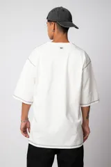 Remera de corte oversize color malva, confeccionada en algodón pesado, con costuras externas visibles en color blanco que recorren el centro, el cuello y los bordes de las mangas.