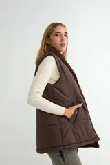 Chaleco acolchado color chocolate con interior y cuello de corderito sintético. Presenta cierre frontal con botones a presión y bolsillos laterales.