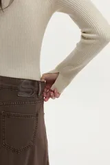 Cardigan tejido en rib con hilado de lurex, color crudo, calce al cuerpo, cuello polo, mangas largas con aberturas y cierre metálico frontal bidireccional.