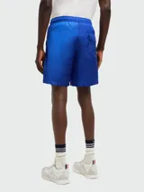 Short de baño azul con cintura elástica y cordón ajustable. Presenta una franja tricolor (rojo, negro y blanco) en el lateral y el logo de la marca en el ruedo.