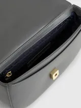 Bandolera gris con solapa y cierre a presión. Presenta una correa ajustable y una cadena dorada gruesa en la parte delantera con el monograma TH.