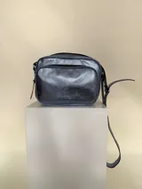 Bandolera rectangular de cuero azul metalizado con correa larga regulable. Cuenta con un bolsillo frontal con fuelle y un bolsillo trasero con cierre.