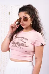 Remera marrón de corte ajustado tipo baby tee, manga corta y cuello redondo, con estampado frontal en blanco de un tren y la leyenda 'Strive to be better Boston'.