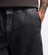 Bermuda de jeans de hombre, color negro con efecto desgastado o acid wash, de corte holgado. Posee cintura elástica con cordón de ajuste y bolsillos laterales.