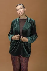 Blazer de terciopelo en color verde profundo, con solapas anchas, cierre frontal con un botón y bolsillos laterales con solapa. Presenta un corte relajado y estructura fluida.