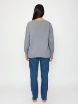 Buzo de punto color gris, con cuello redondo y diseño de textura sutil en la parte superior. Presenta mangas largas con puños acanalados y ruedo también acanalado, con un corte recto y holgado.