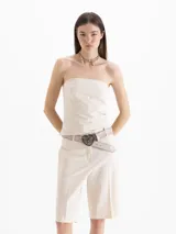 Top strapless de color beige, estilo corsé, ajustado al cuerpo con diseño estructurado y sutiles aberturas laterales en el dobladillo.