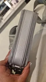 Cartera tipo bandolera de diseño rectangular y estructura rígida, color gris. Cuenta con doble compartimento superior con cierre metálico, herrajes plateados y correa de hombro ancha, ajustable y extraíble.