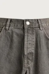 Jeans loose fit de hombre en denim de algodón color gris oscuro con efecto lavado. Presenta perneras con costuras giradas hacia los tobillos, tiro medio, cierre frontal con botones y bolsillos frontales con bolsillo cerillero.
