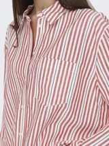 Camisa de manga larga con cuello clásico y cierre frontal de botones. Diseño holgado con bolsillo en el pecho. Estampado de rayas verticales en rojo, blanco y negro.