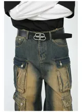 Pantalón de jean ancho (baggy) con lavado oscuro y efecto desgastado en tonos marrones/ocre. Presenta múltiples bolsillos cargo grandes con tapa y botones a presión en las piernas.