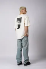 Remera de corte oversize confeccionada en algodón premium de gramaje pesado, color crudo. Presenta un bordado frontal pequeño en el centro del pecho con un diseño de dos árboles unidos por sus raíces y un parche estampado en la espalda con una silueta de mano fusionada con ramas.